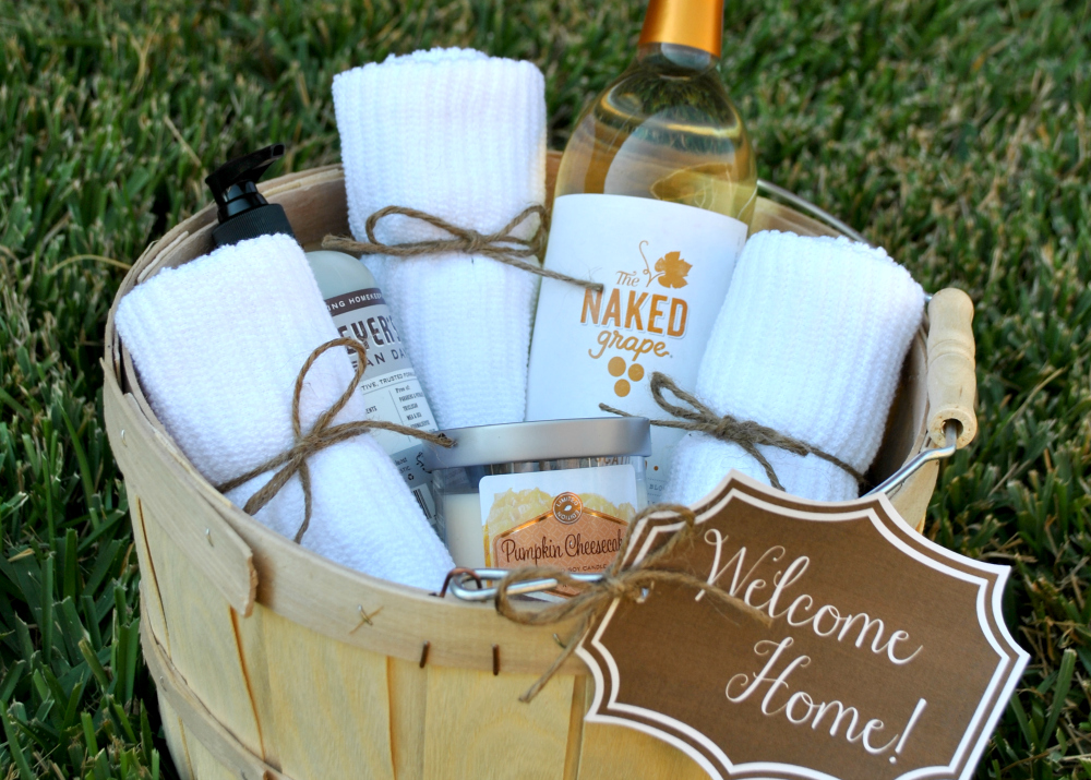 A photograph of a gift basket with a bottle of wine, towels, a scented candle and hand soap and a label that reads welcome home. 