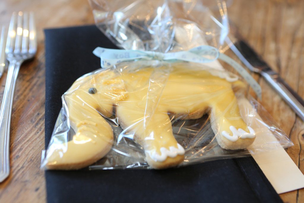 A yellow frosted elephant cookie wrapped in cellophane with a ribbon at a table place setting. 