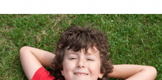 5 Reasons to Redshirt Kindergarten A photograph of a smiling child lying on the grass and wearing a red shirt.