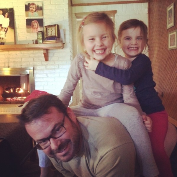 Two smiling children sitting on top of their father's back. 