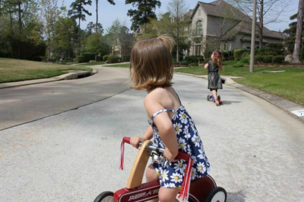 A photograph of a child on a tricycle in a neighborhood.