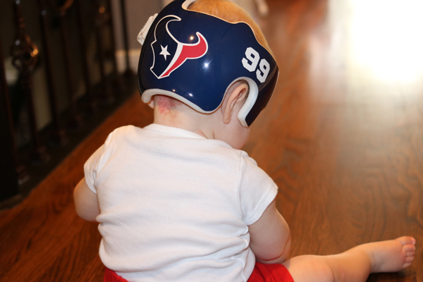 A baby wearing a helmet with the Houston Texans logo and the number 99. 