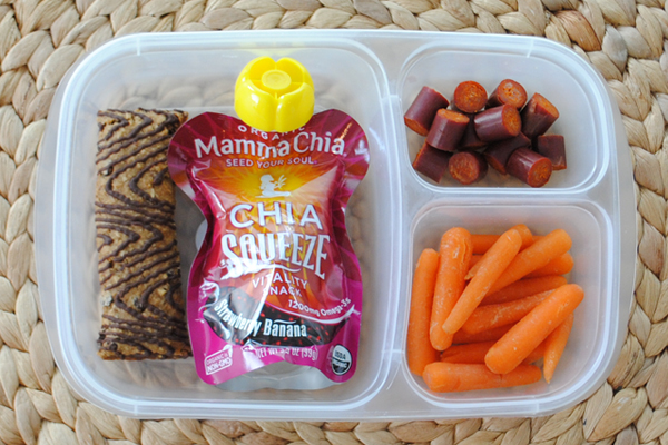A plastic container with three divisions containing A Z bar, a Mamma Chia pouch, a turkey stick and baby carrots. 