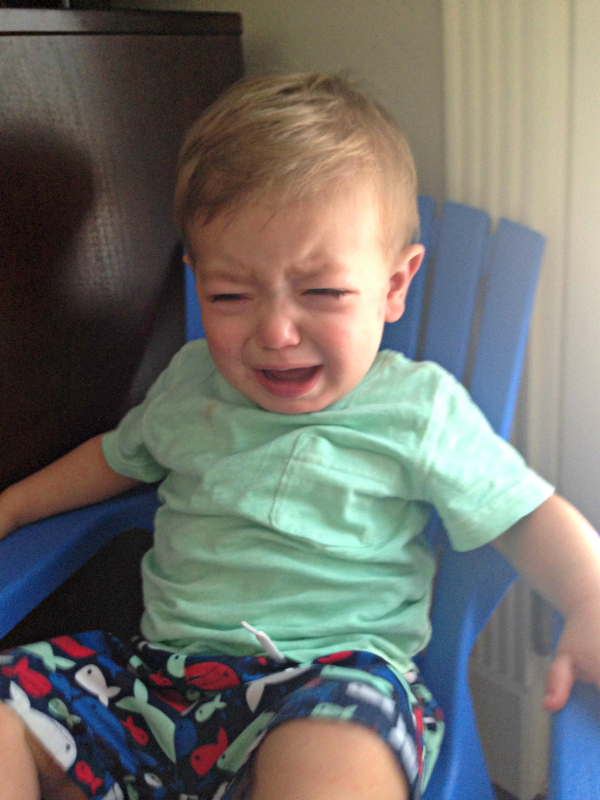 A crying toddler sitting in a small chair. 