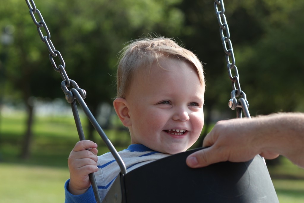 A young smiling child being pushed in a swing. 