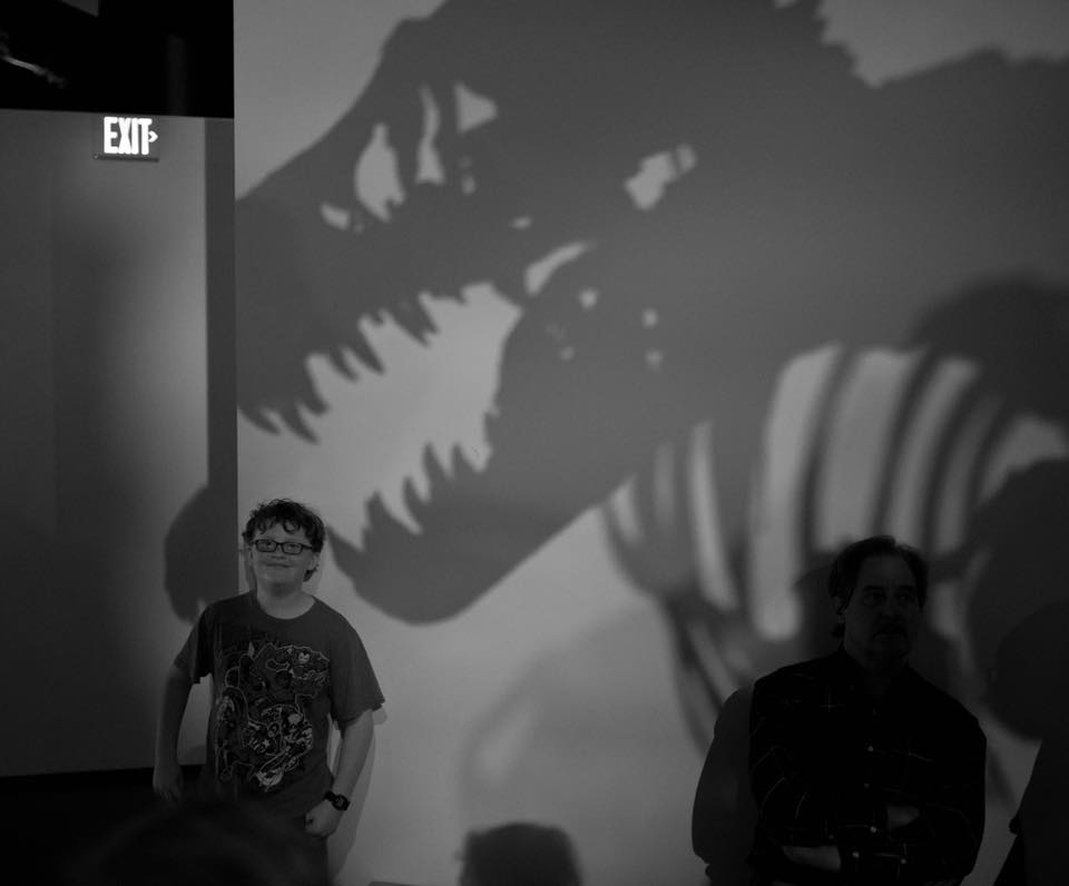 A child standing in front of a dinosaur shadow. 