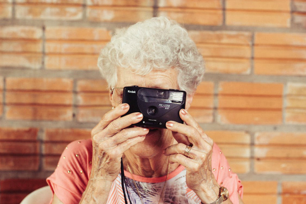 An older mother holding a camera in front of her face.