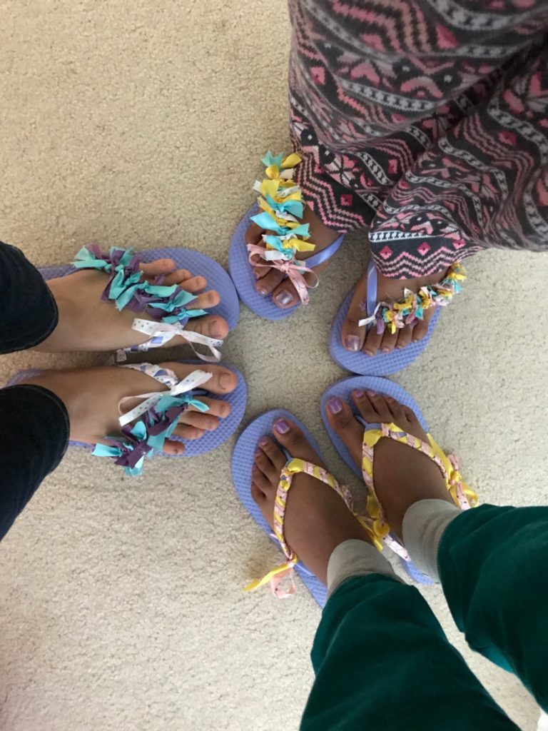 Three pairs of feet each wearing flipflops decorated with ribbons. 