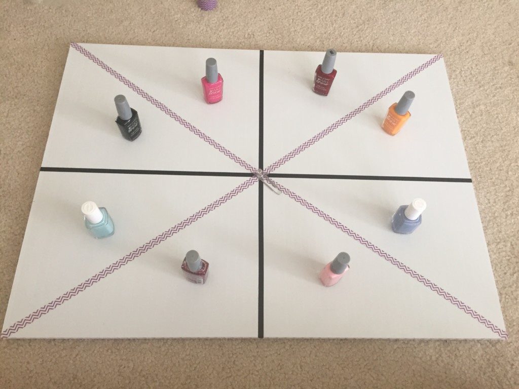 A project display board divided into 8 sections. Each section contains one bottle of nail polish. A spinner is at the center of the board. 