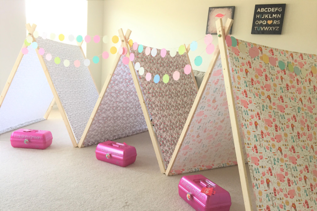Three adjacent tents set up in carpeted room and connected by bunting. In front of each tent is a child's organization box. 