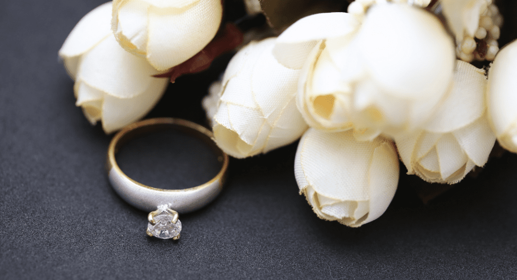 Fabric white roses next to a diamond ring. 