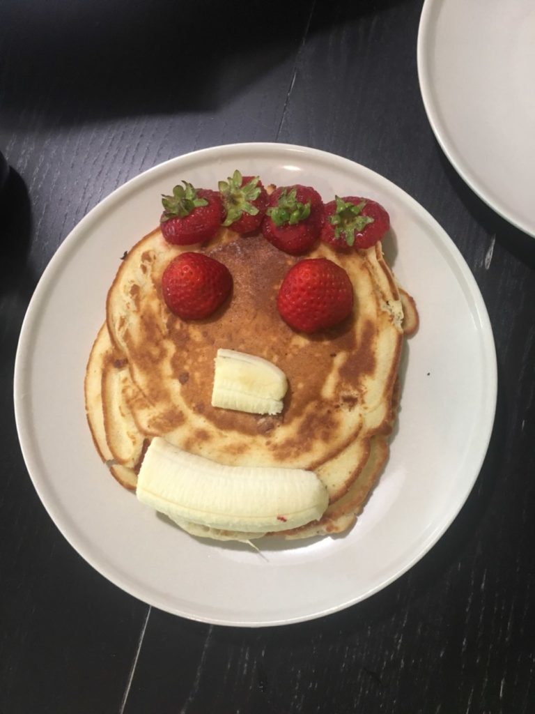 A plate of pancakes with facial features created from fruit. 