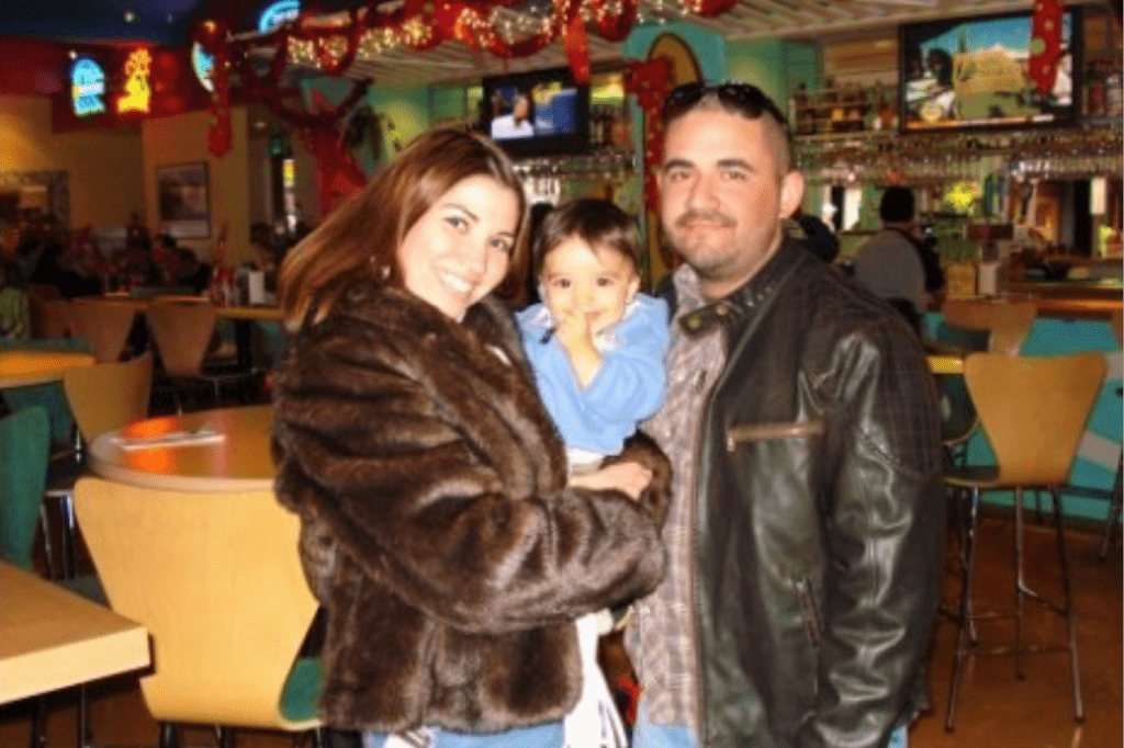 A smiling man and woman holding a child at a restaurant. 