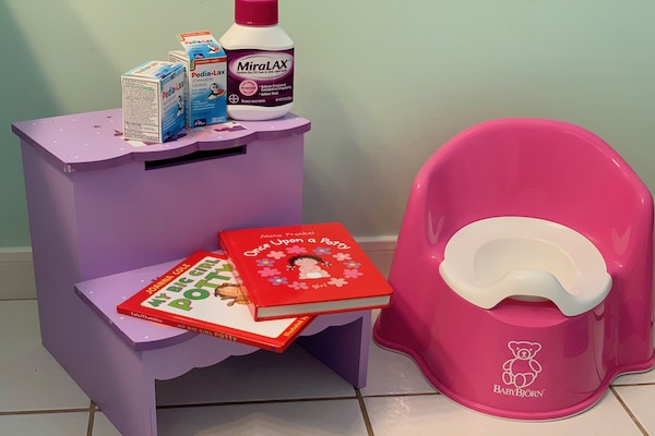 A photograph of a child's training toilet, children's books, a bottle of Miralax and two juice containers.