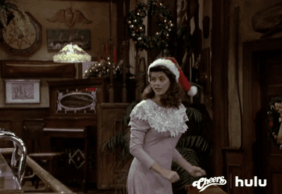 A GIF of a happy women wearing a Santa hat smiling, jumping and clapping her hands. 