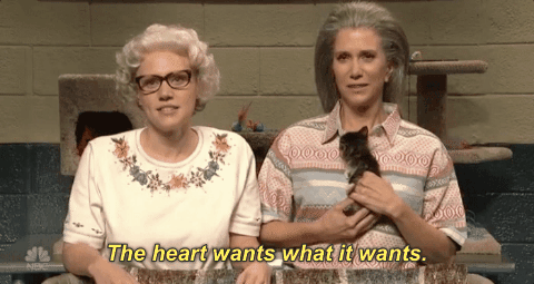 A GIF of two women. One is holding a kitten. Text states: The heart wants what it wants. 