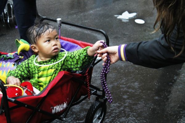 child in stroller being handed Mardi Gras beads
