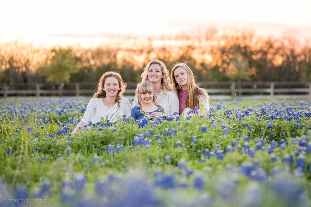 A mother and three children sitting together in a field of Bluebonnets. 