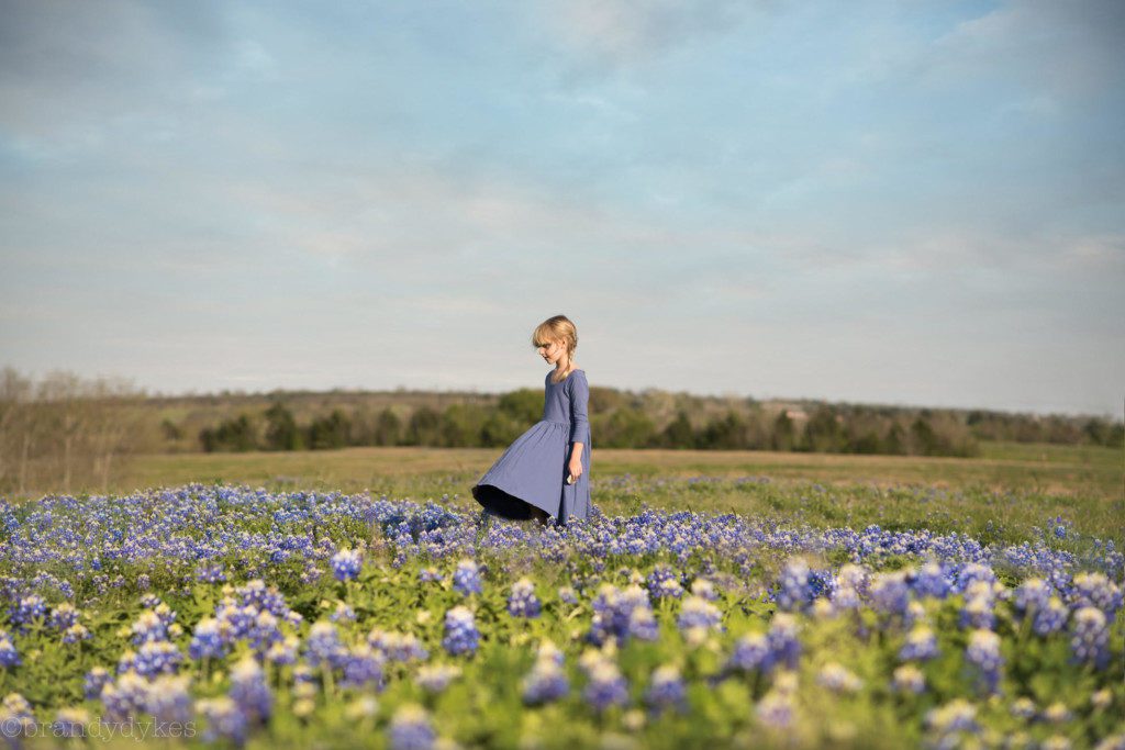 A young girl standing in a field of bluebonnets. 