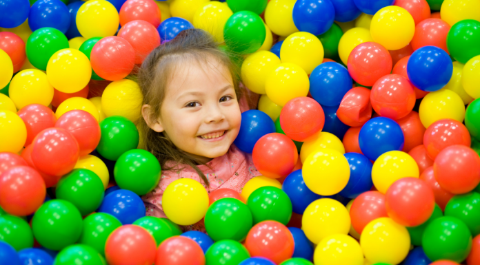 A smiling young child in a toy ball pit.