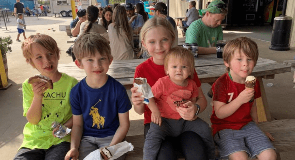 Five children sitting at a picnic bench and eating ice cream. 