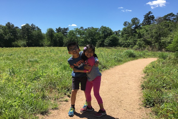 Two smiling children hugging each other on a trail.