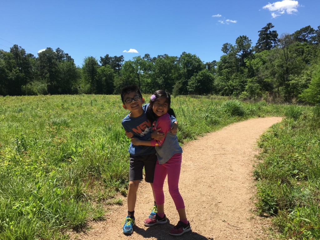 Two smiling children hugging each other on a trail. 