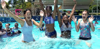 A photograph of four smiling teenage girls jumping in a pool at a waterpark