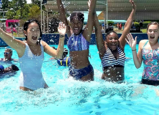 A photograph of four smiling teenage girls jumping in a pool at a waterpark