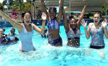 A photograph of four smiling teenage girls jumping in a pool at a waterpark