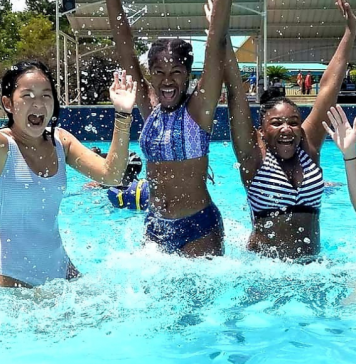 A photograph of four smiling teenage girls jumping in a pool at a waterpark