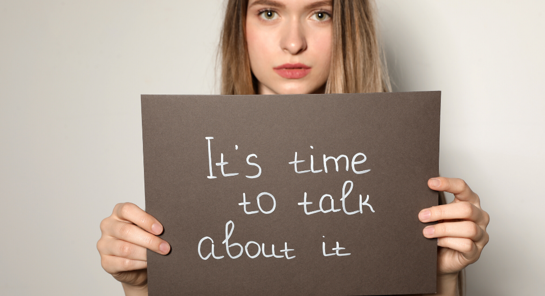 A woman holding a sign with the text: It's time to talk about it.