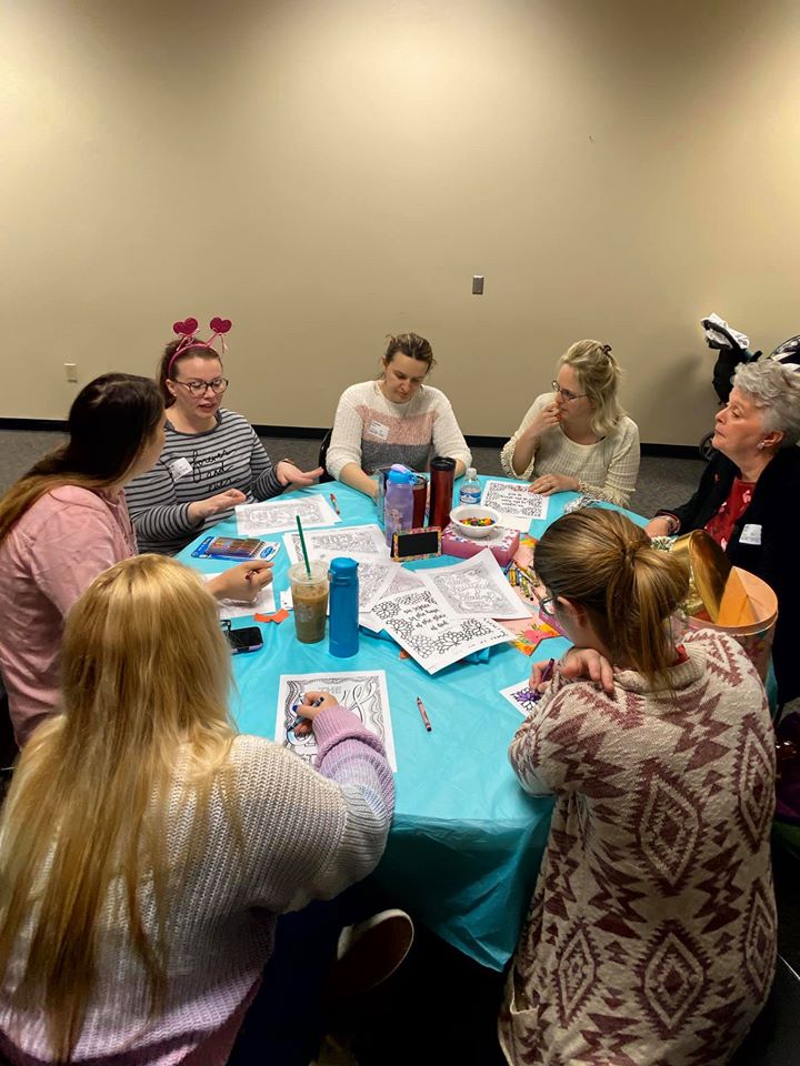 7 mothers sitting around a table and coloring in adult coloring books. 