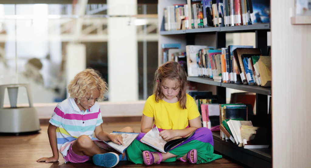 Two children sitting on a library floor and reading.