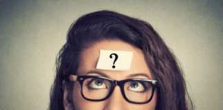 A photograph of a woman looking up at a question mark stuck to her forehead.