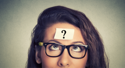 A photograph of a woman looking up at a question mark stuck to her forehead.