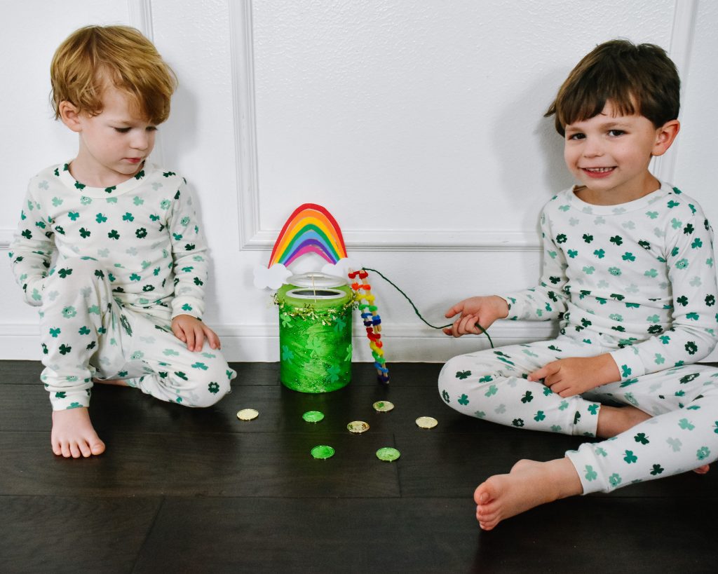 two boys in shamrock pajamas sit on floor beside Leprechaun trap