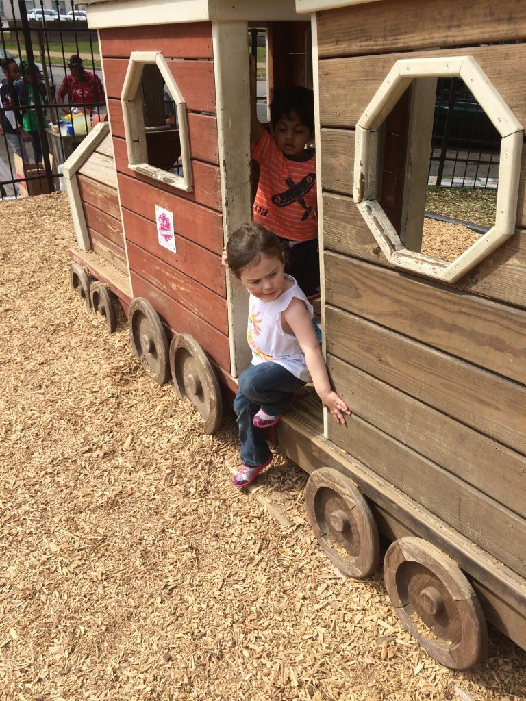 Two children playing inside a wooden train in a playground. 