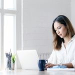 Portrait of young businesswoman looking at laptop screen while sitting at office desk in modern office.