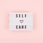 Self-care word on lightbox and flower narcissus on pink background flat lay. Take care of yourself.