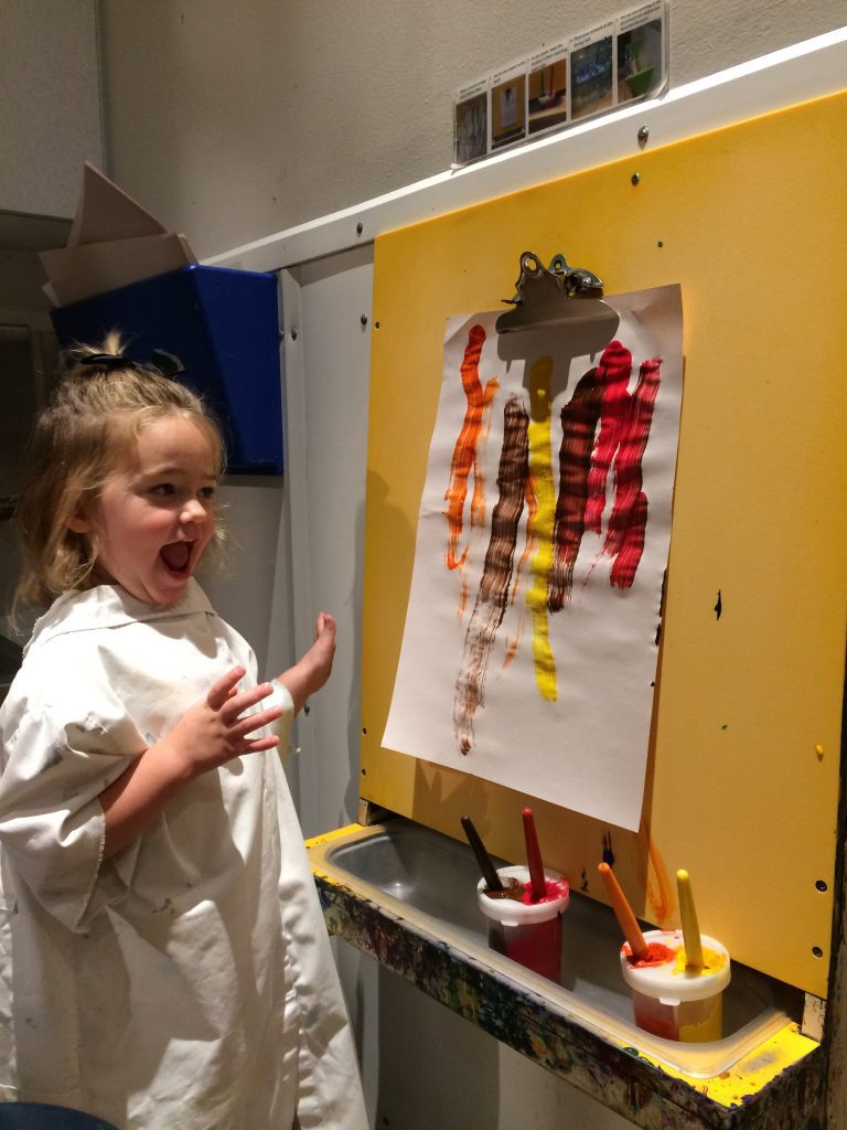 A happy child wearing a smock and painting at an easel. 