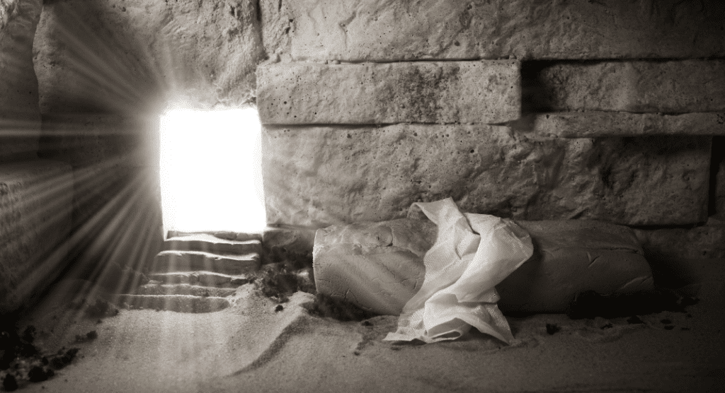 A room made of stone with light coming in a doorway and a shroud on a stone. 