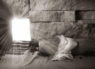 A room made of stone with light coming in a doorway and a shroud on a stone.