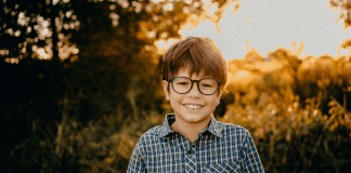 A photograph of a smiling boy standing outside.