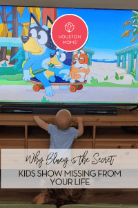 Why Bluey is the Secret Kids Show Missing From Your Life. Logo: Houston Moms. A photograph of a baby and a young child watching Bluey on a TV at home.