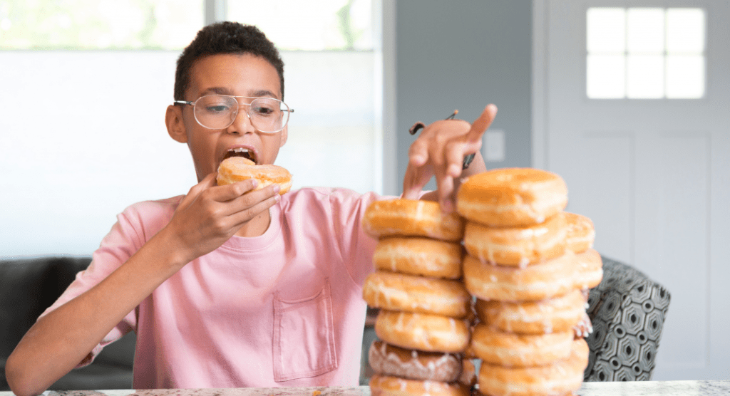 young boy holds a donut while looking at a plate stacked with donuts