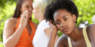 A sad woman in front of two women gossiping in the background.