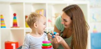 A mother playing with a toddler with a stacked ring toy.