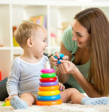 A mother playing with a toddler with a stacked ring toy.