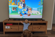 A baby and a young child watching Bluey on a TV at home.
